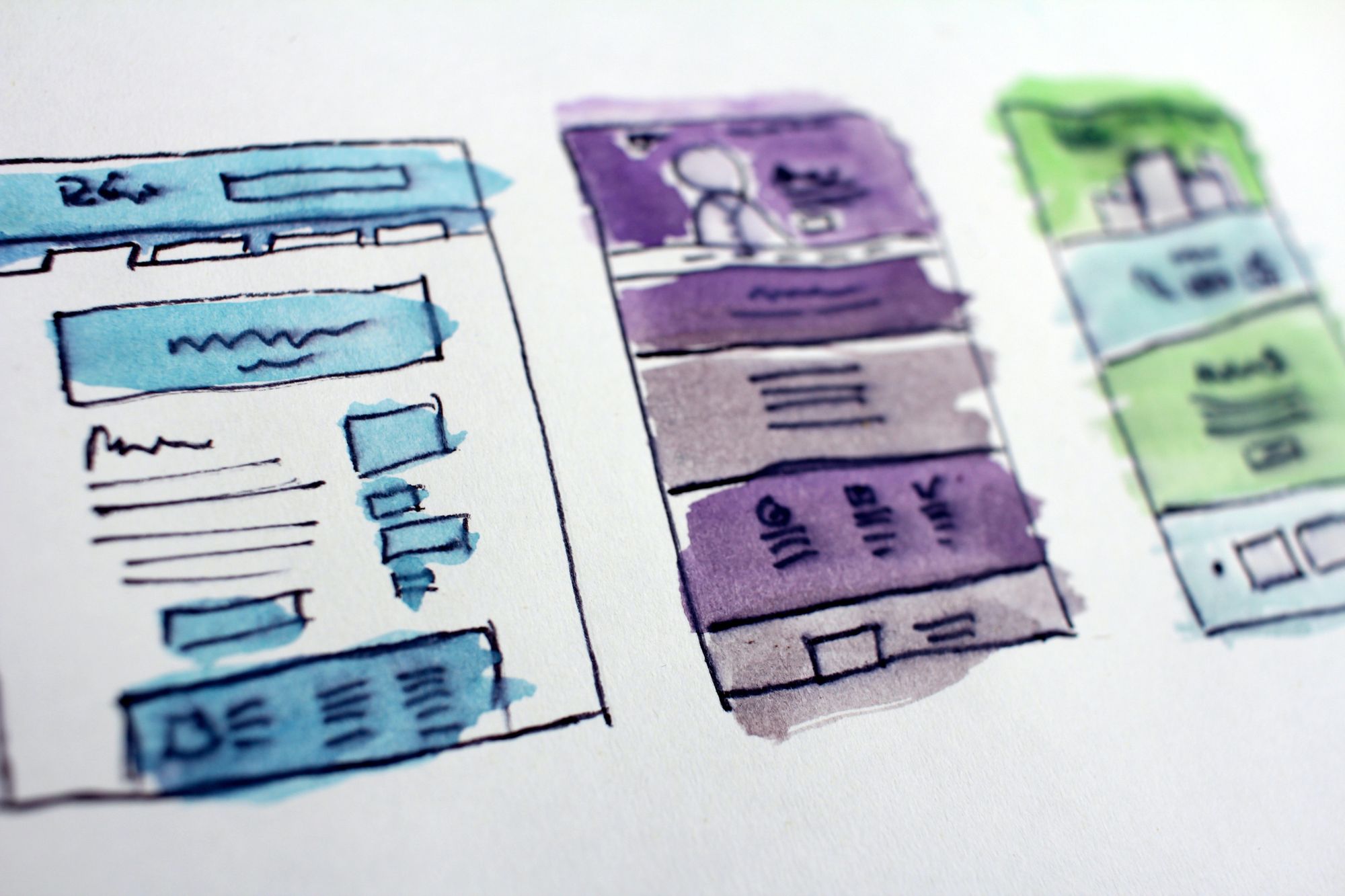 Stock image of a very rough drawing and water colour sketch of three different website interfaces - one is blue, one is purple, and one is green.