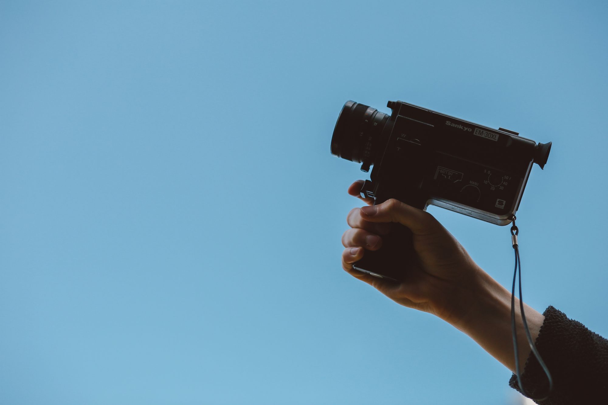 Stock image of a hand holding an old film camera with a blue background